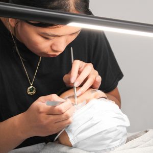Classic lash extensions being applied to woman's eyelashes with tweezers.