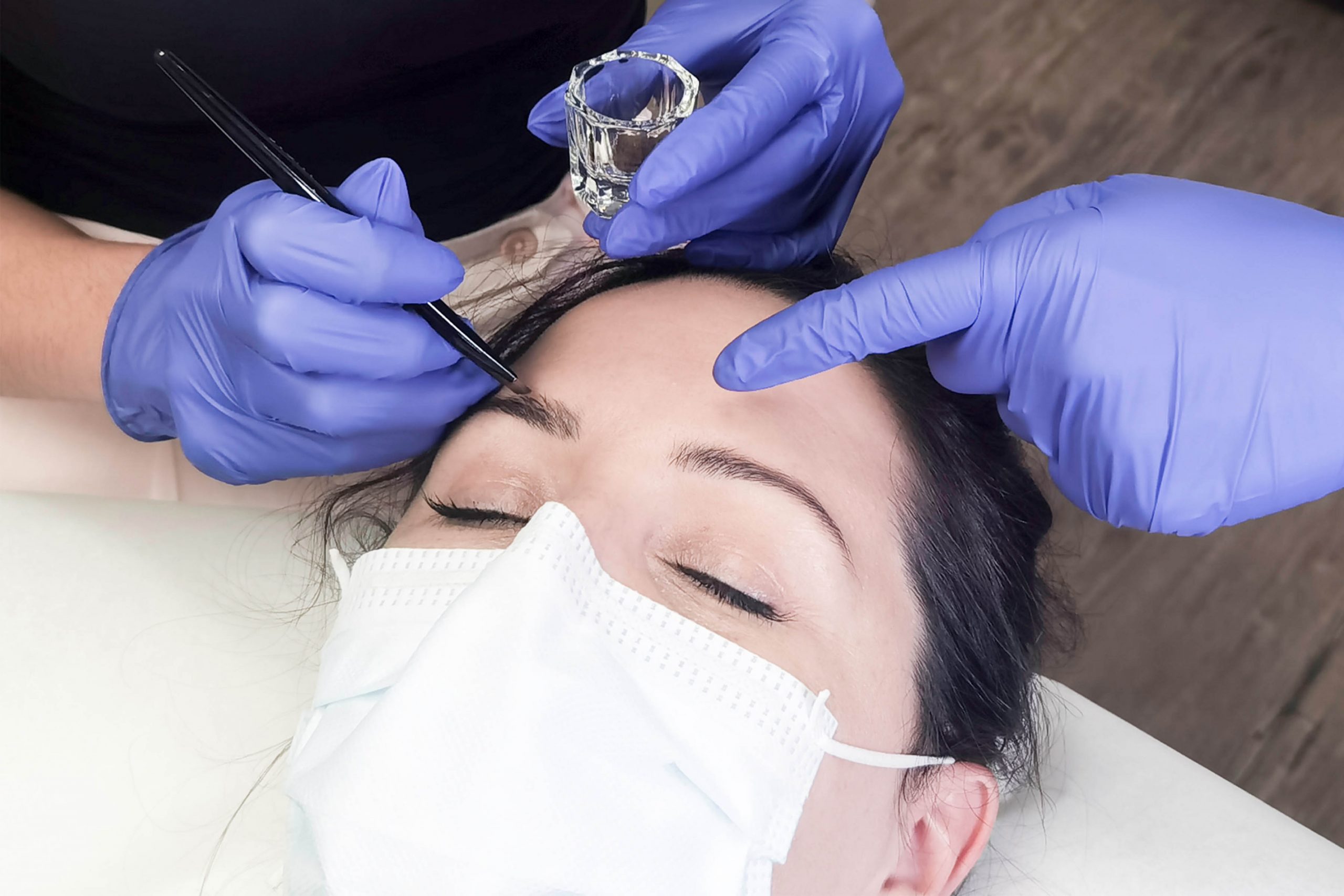 Gloved hands performing brow waxing treatment on client