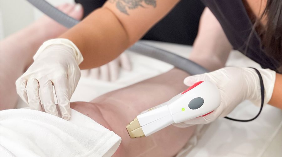 student holding laser hair removal hand piece to a client's knee