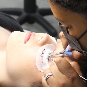 Student applying lash extensions to client's eyelashes using tweezers.