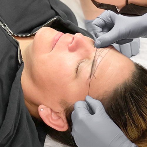 Hands holding brow mapping thread against client's eyebrows
