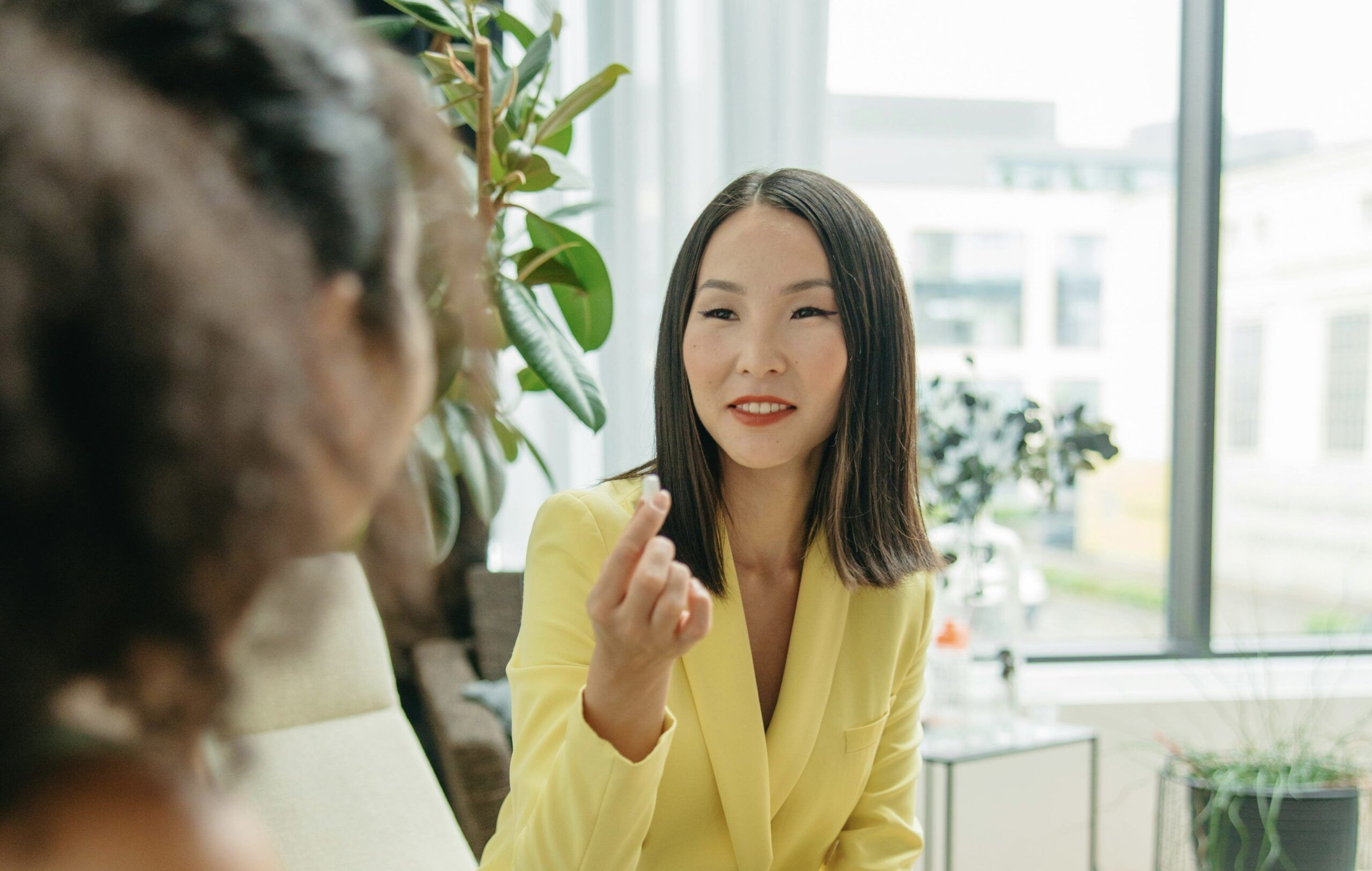 Client in a yellow blazer talking to an esthetician about possible contraindications to receiving a facial treatment