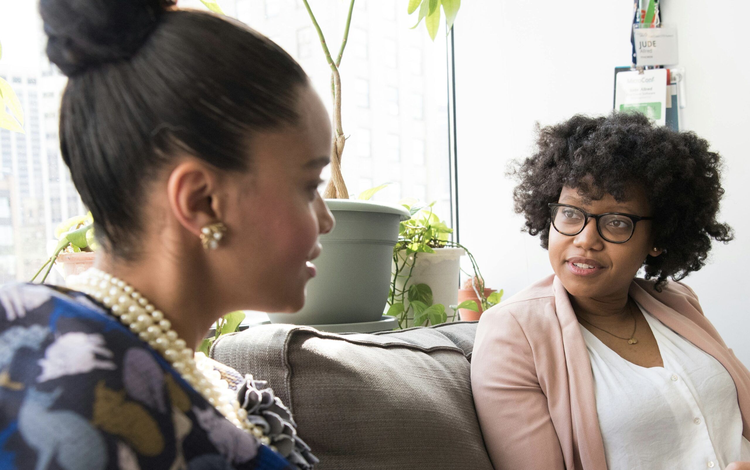 Client in a pearl necklace talking to an esthetician in a white top with a pink blazer
