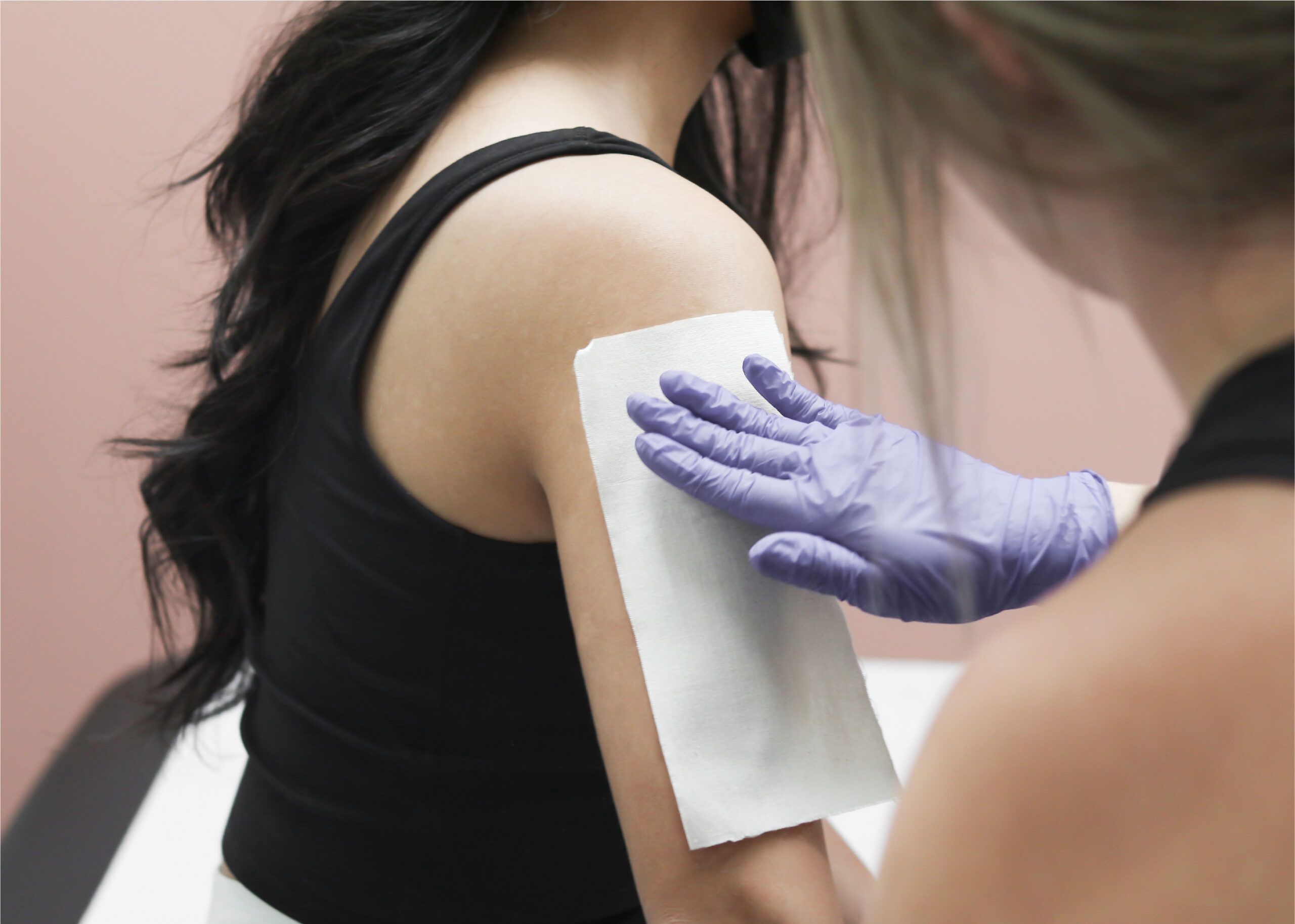 Student applying body waxing strip to client's upper arm