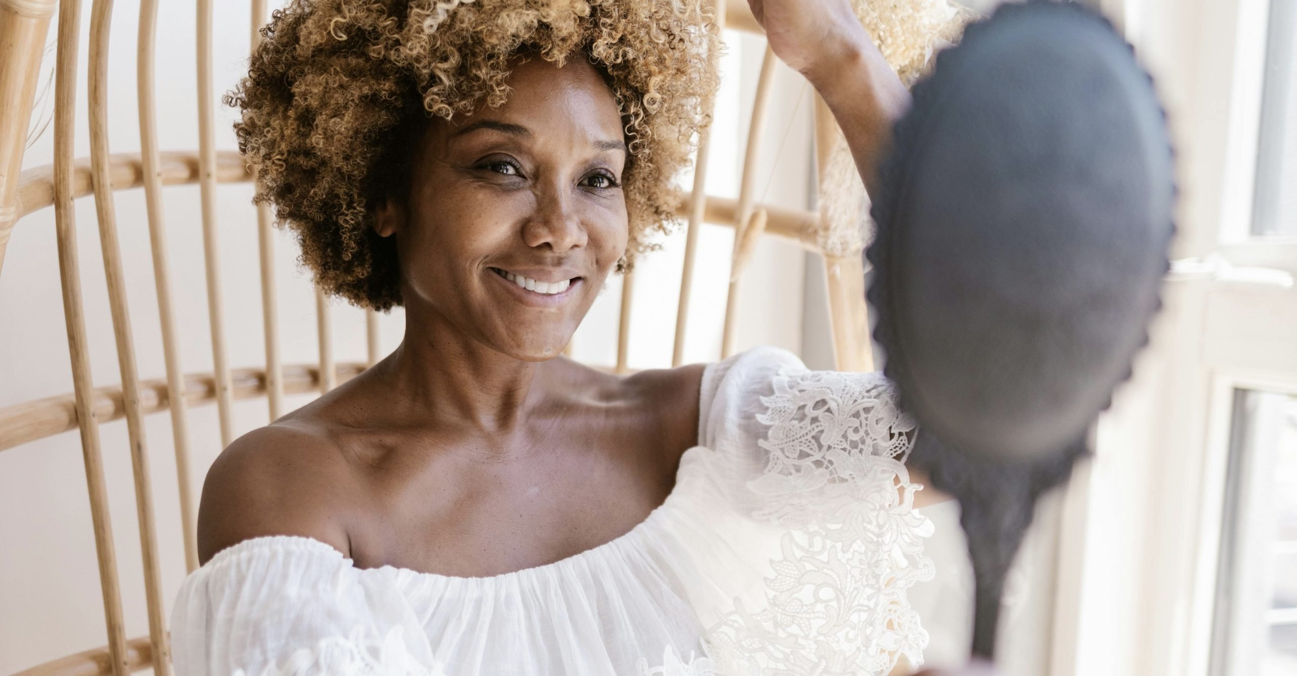 A woman looking in the mirror, smiling, and feeling a renewed sence of confidence after a facial with her skin technician